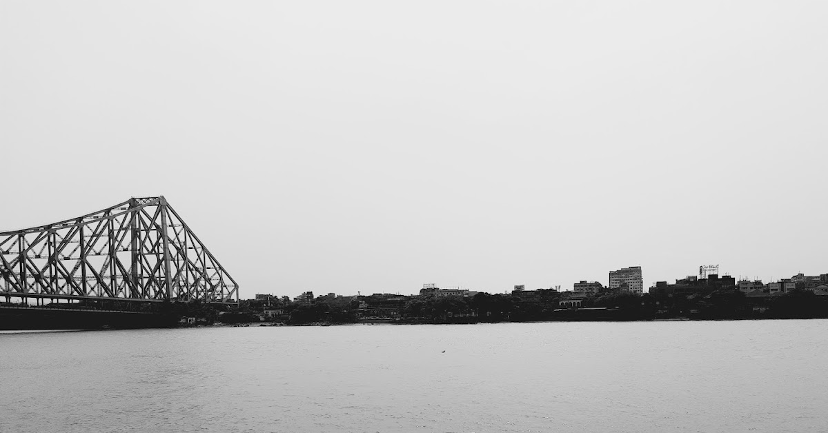 A black-and-white photograph of the Howrah Bridge across the Hooghly river in Kolkata